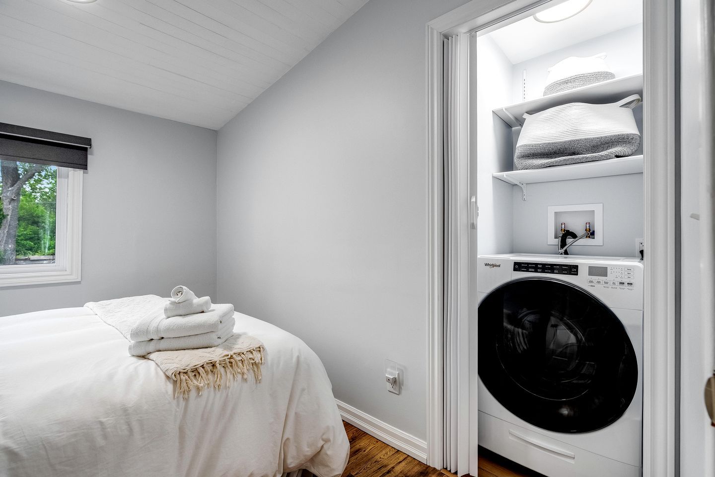 A bedroom with a bed, a washing machine, and a window.