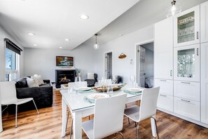 A modern kitchen with white cabinetry, a dining table set for four, and a fireplace. - Gorgeous Cottage with Fire Pit and Nice Beach Vistas in Leamington, Ontario (Leamington)