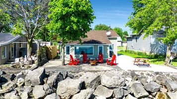 A residential area with a house featuring a patio with red Adirondack chairs, a stone wall in the foreground, and a clear blue sky.