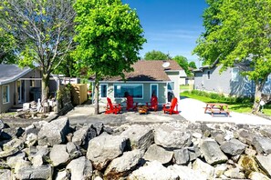 Et boligområde med et hus, en terrasse med røde Adirondack-stole, en stenvæg i forgrunden og en klar blå himmel.
