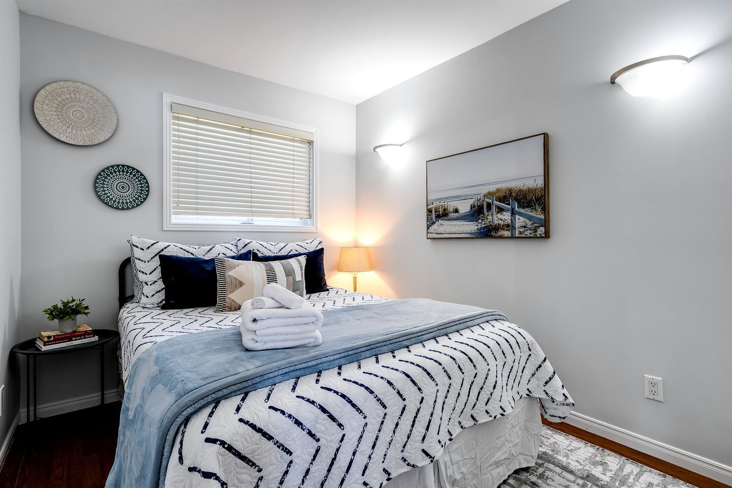 Un dormitorio ordenado con cama, mesitas de noche, lámpara y adornos en la pared.