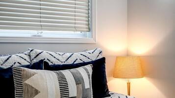 A bedroom with a bed, pillows, a lamp, and a window with blinds.