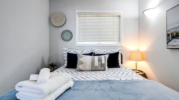 Ein Schlafzimmer mit Bett, Kissen, einer Nachttischlampe, einem Fenster mit Jalousien und Wanddekoration.