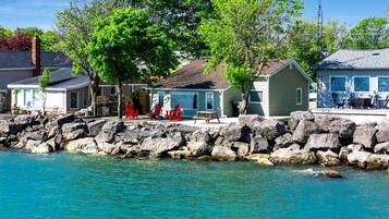 A waterfront property with a rocky shoreline, a covered patio with red chairs, and a small building with a sloped roof.