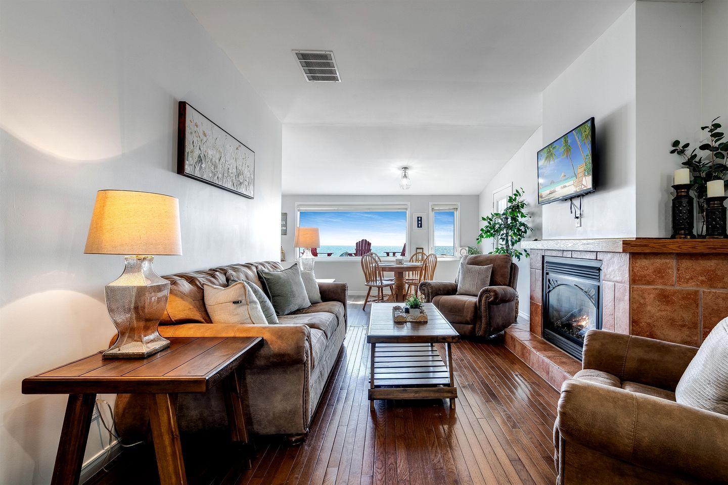 Sala de estar com sofá, poltronas, mesa de centro, lareira e área de jantar com vista para o oceano.