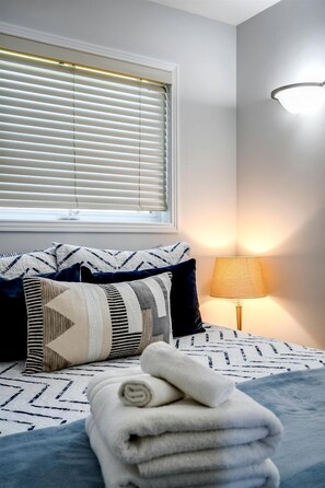 A bedroom with a bed, pillows, a lamp, and a window with blinds.