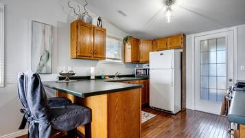 A kitchen with wooden cabinets, a white refrigerator, a dining area with a chair, and a window with blinds.