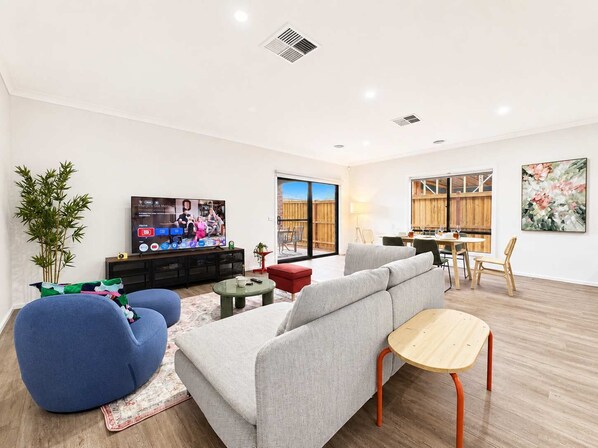 A modern living room with a sofa, armchair, and a television. - Modern 4BR Gateway to Great Ocean Rd and Geelong (Armstrong Creek)