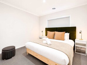 A modern hotel room with a large bed, two bedside tables, a small ottoman, and a headboard with a mirror. - Modern 4BR Gateway to Great Ocean Rd and Geelong (Armstrong Creek)