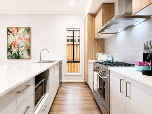 A modern kitchen with white cabinetry, stainless steel appliances, and a wooden door. - Modern 4BR Gateway to Great Ocean Rd and Geelong (Armstrong Creek)