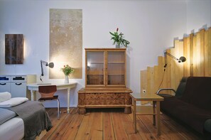 Ein Zimmer mit einem Bett, einem Schreibtisch, einem Schrank, einem Stuhl, einer Couch und einer Holztreppe.