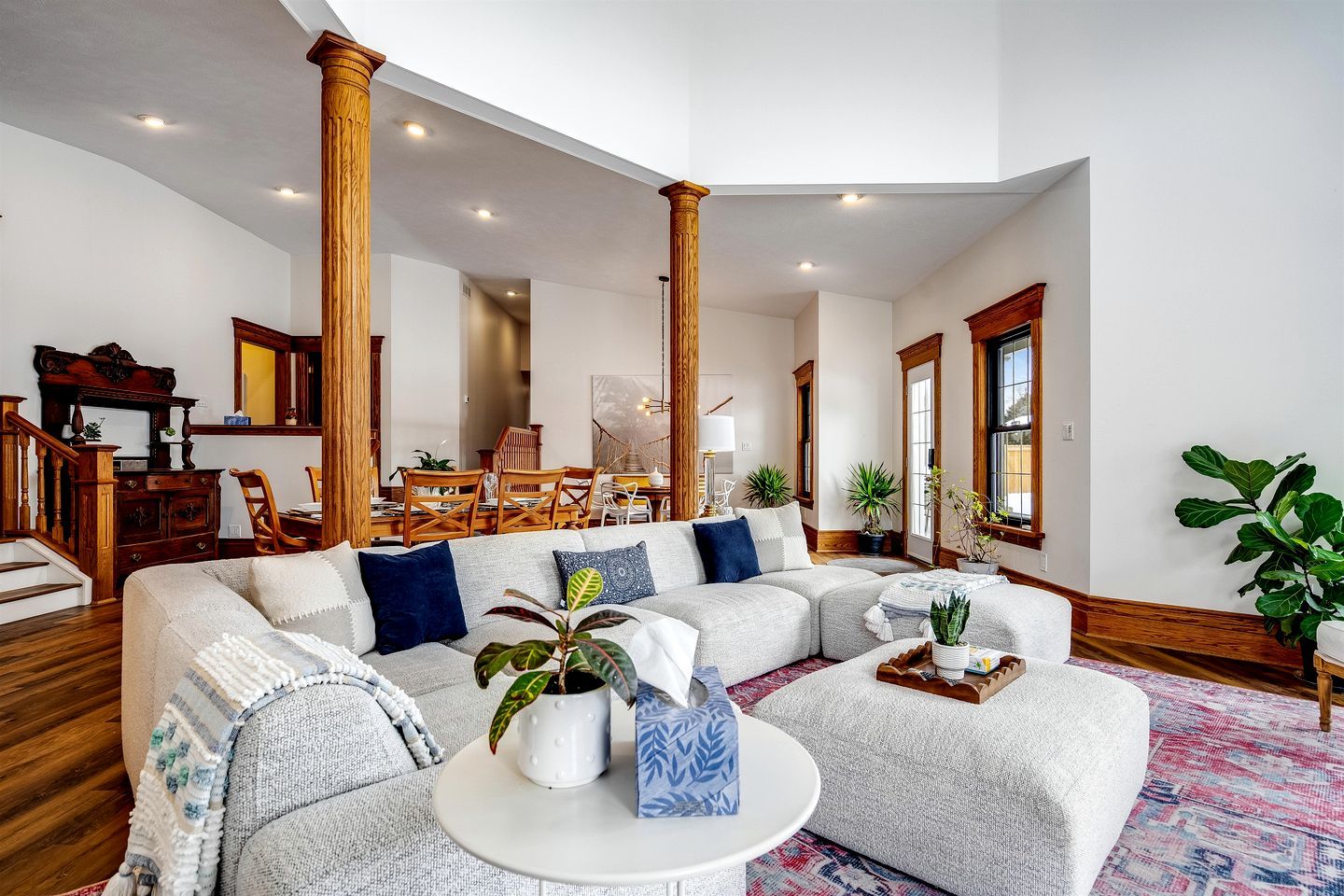 A spacious living room with a large sectional sofa, wooden columns, and a dining area with wooden furniture.