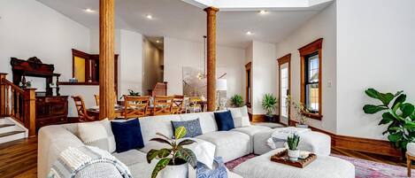 A spacious living room with a large sectional sofa, wooden columns, and a dining area with wooden furniture.