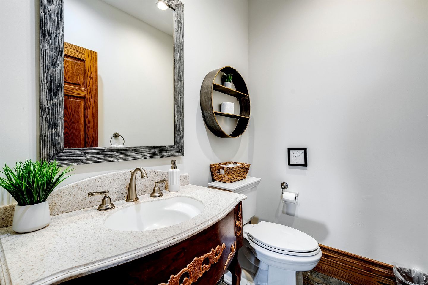 A bathroom with a large mirror, a sink with two faucets, a toilet, and a shelf with a basket.