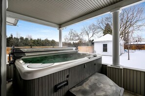 A hot tub in a covered outdoor area with a view of a snowy yard and a house. - Luxurious Vacation Rental near Lake Erie for an Amazing Family Retreat in Leamington, Ontario (Leamington)