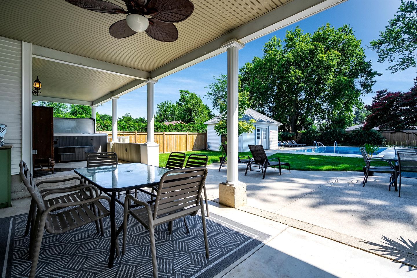 A covered patio with a table and chairs, a pool, and a backyard with a fence and trees.