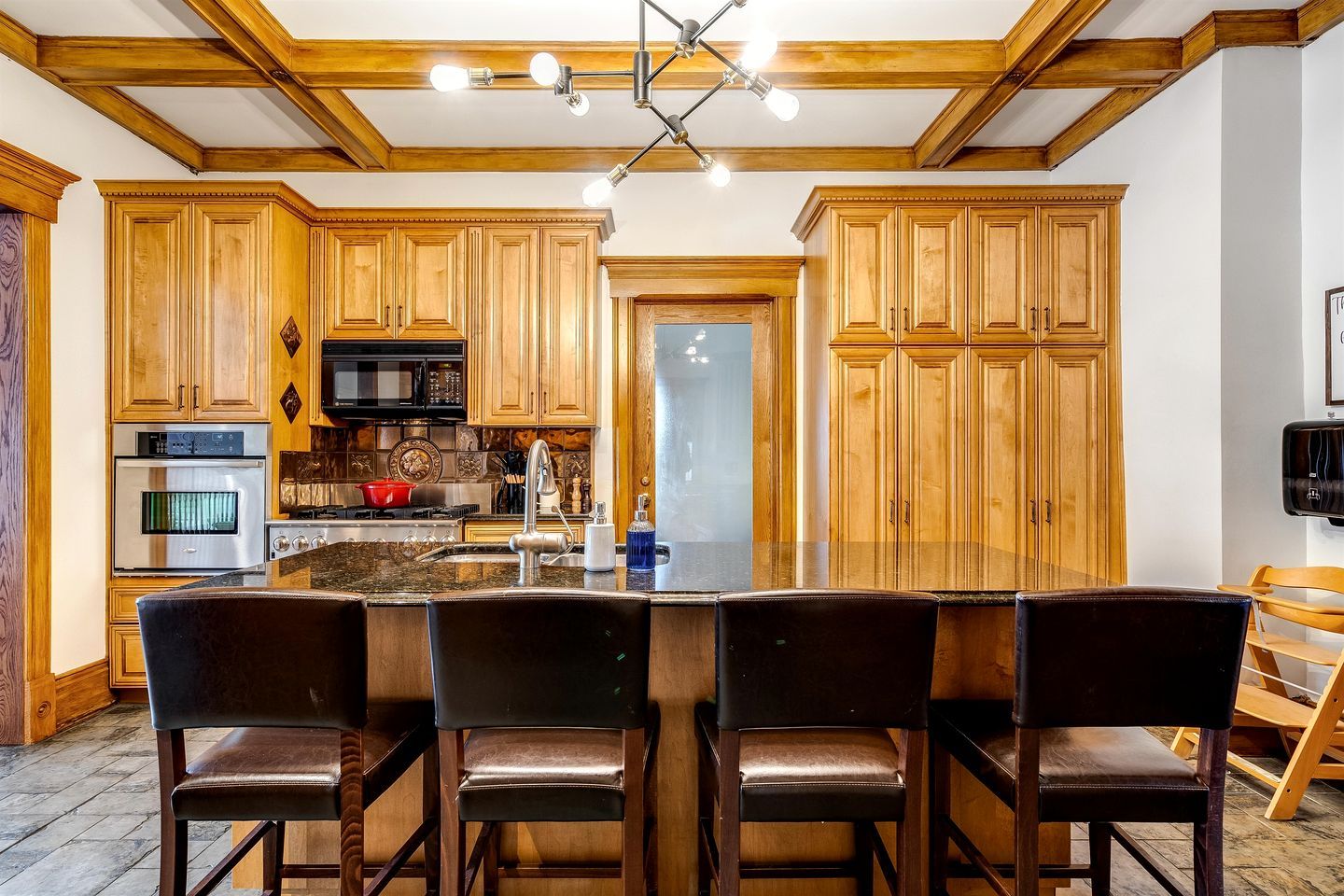 A kitchen with wooden cabinets, a central island with bar stools, a microwave, oven, and a refrigerator.