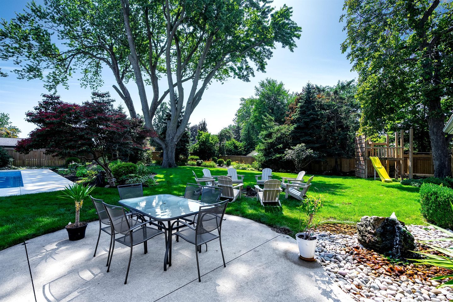 Un jardin avec une table et des chaises de patio, une petite piscine et une aire de jeux pour enfants.