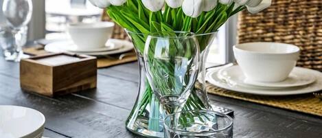 Une table à manger ornée d’un vase de tulipes blanches, de verre transparent et d’assiettes blanches.