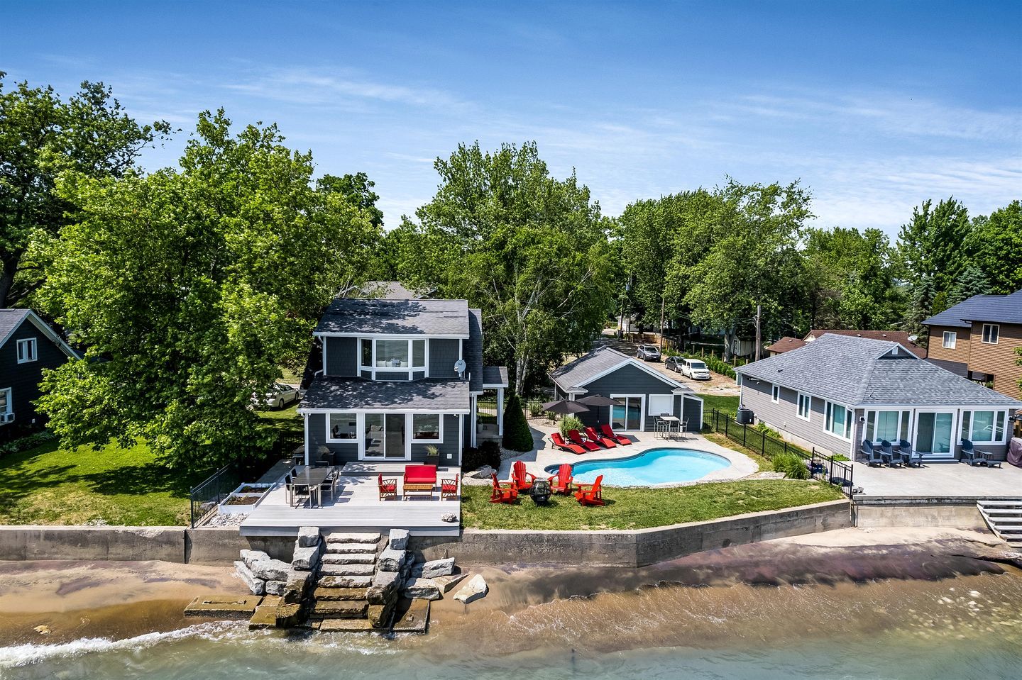 A two-story house with a swimming pool, outdoor seating, and a dock extending into a body of water.