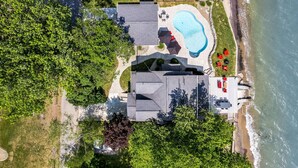 Vista aérea de una propiedad costera con piscina, un patio con mobiliario exterior y una zona de playa.