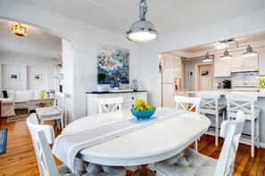 Eine moderne Küche mit weißen Schränken, ein Essbereich mit rundem Tisch und ein Wohnzimmer mit Sofa und Sesseln.