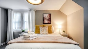 Ein Hotelzimmer mit einem großen Bett, einem Nachttisch mit Lampe, einem Fenster mit Vorhängen und einem Gemälde an der Wand.