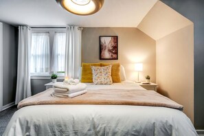 A hotel room with a large bed, a bedside table with a lamp, a window with curtains, and a painting on the wall. - Peaceful Cottage with Hot-Tub and Breathtaking Views in Ontario (Leamington)