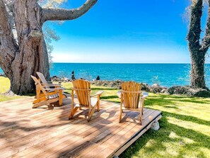 A wooden deck with three Adirondack chairs facing a clear blue sea. - Peaceful Cottage with Hot-Tub and Breathtaking Views in Ontario (Leamington)