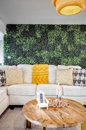 A living room with a sofa, decorative pillows, a wooden coffee table, a remote control, and a wall-mounted light fixture. - Peaceful Cottage with Hot-Tub and Breathtaking Views in Ontario (Leamington)