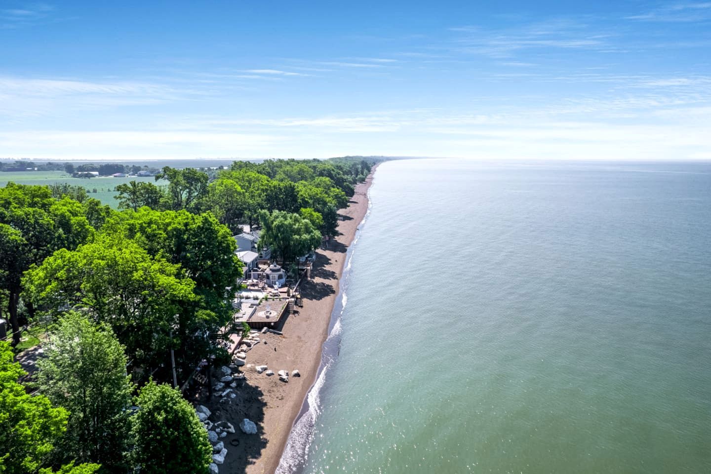 Una vista aerea di una spiaggia con una fila di edifici lungo la riva, immersa nel verde.