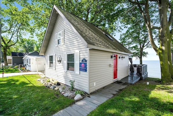 A small, single-story cabin with a red door, a small porch, and a sign indicating it is a short-term rental.