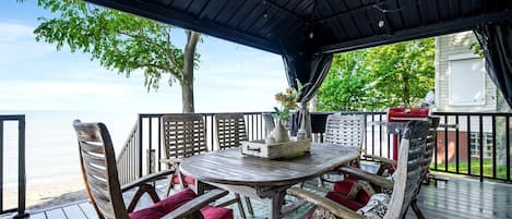 A covered outdoor seating area with a table and chairs, overlooking a body of water.