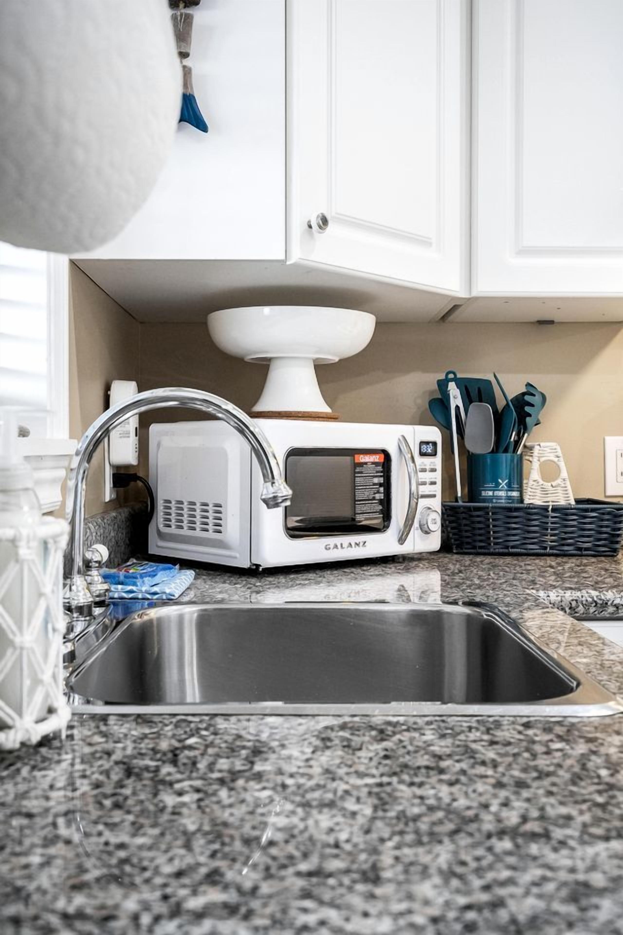 Una cucina con forno a microonde integrato, lavello in acciaio inossidabile e mobiletto bianco.