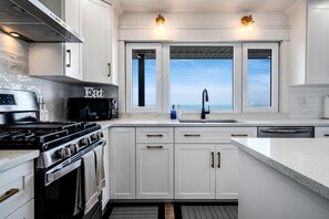 A modern kitchen with white cabinetry, a stove, a microwave, and a large window offering a view. - Charming Lakefront Vacation Rental on Lake Erie for a Memorable Family Escape in Leamington, Ontario (Leamington)