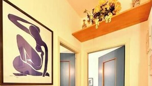 Ein Flur mit einem gerahmten abstrakten Kunstwerk, einem Holzregal mit Dekorationen und einer Tür, die in ein Schlafzimmer führt.