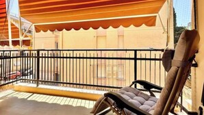 Ein Balkon mit gestreifter Markise, einem gepolsterten Stuhl und einem Metallgeländer.