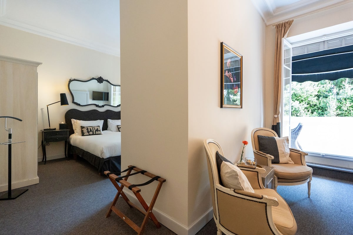 A hotel room with a bed, a chair, a desk, a lamp, a mirror, and a window with a view.