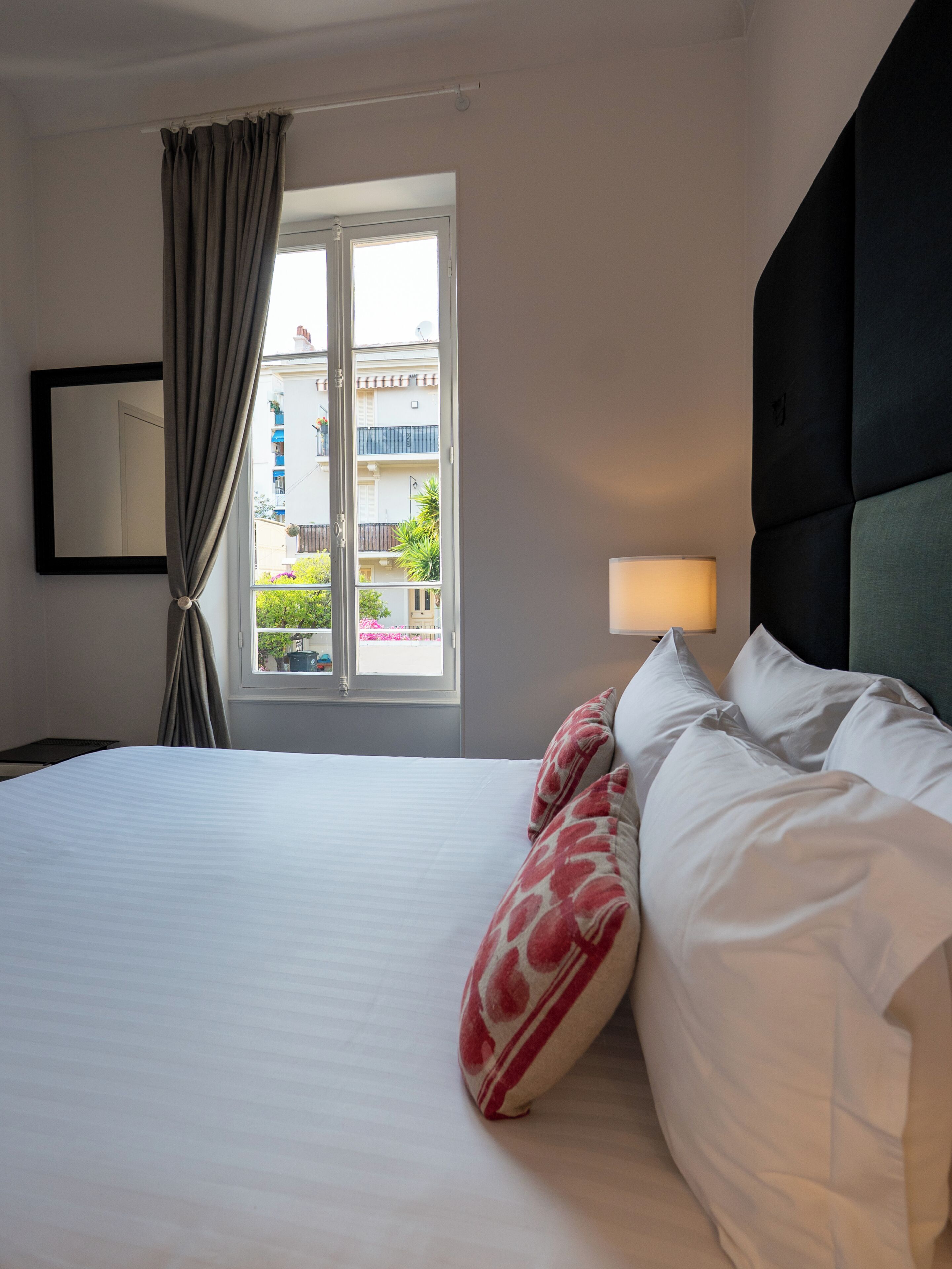 A hotel room with a bed, a window with curtains, a bedside lamp, and a view of the outside.