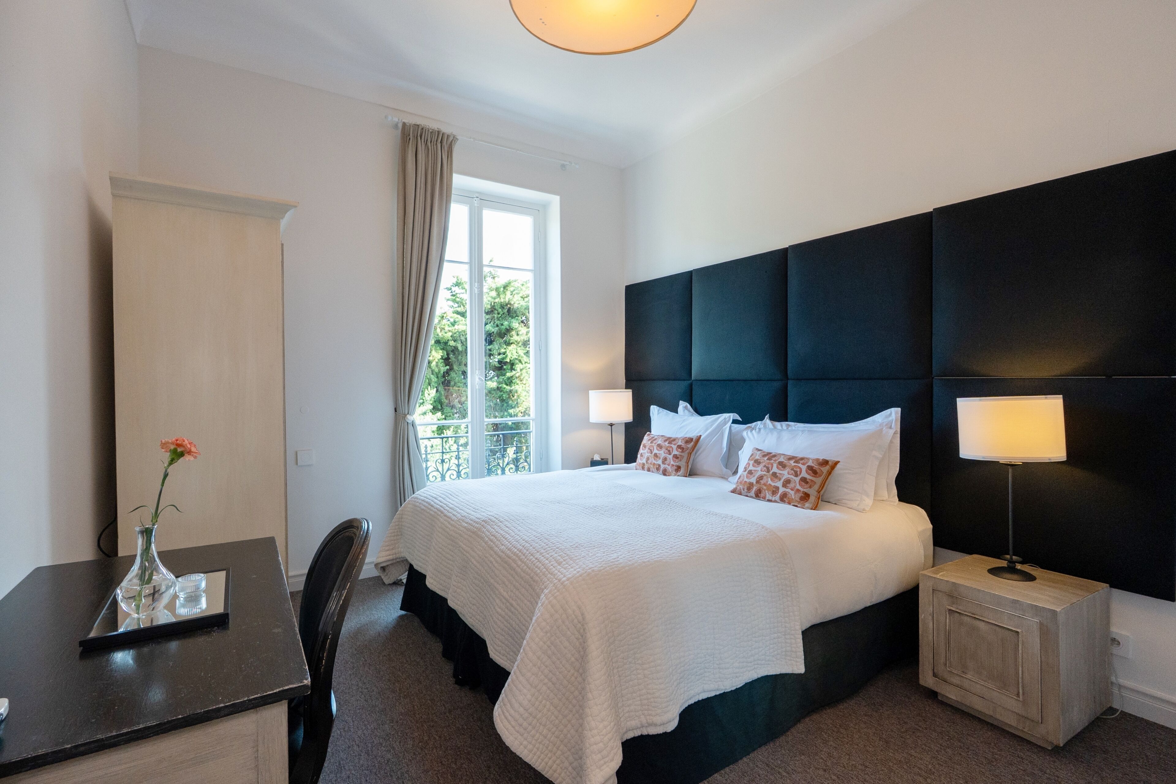 Habitación de hotel con cama, mesita de noche, lámpara, silla y ventana con cortinas.