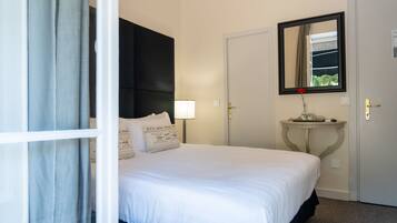A hotel room with a bed, a bedside table with a lamp, a mirror, and a door.