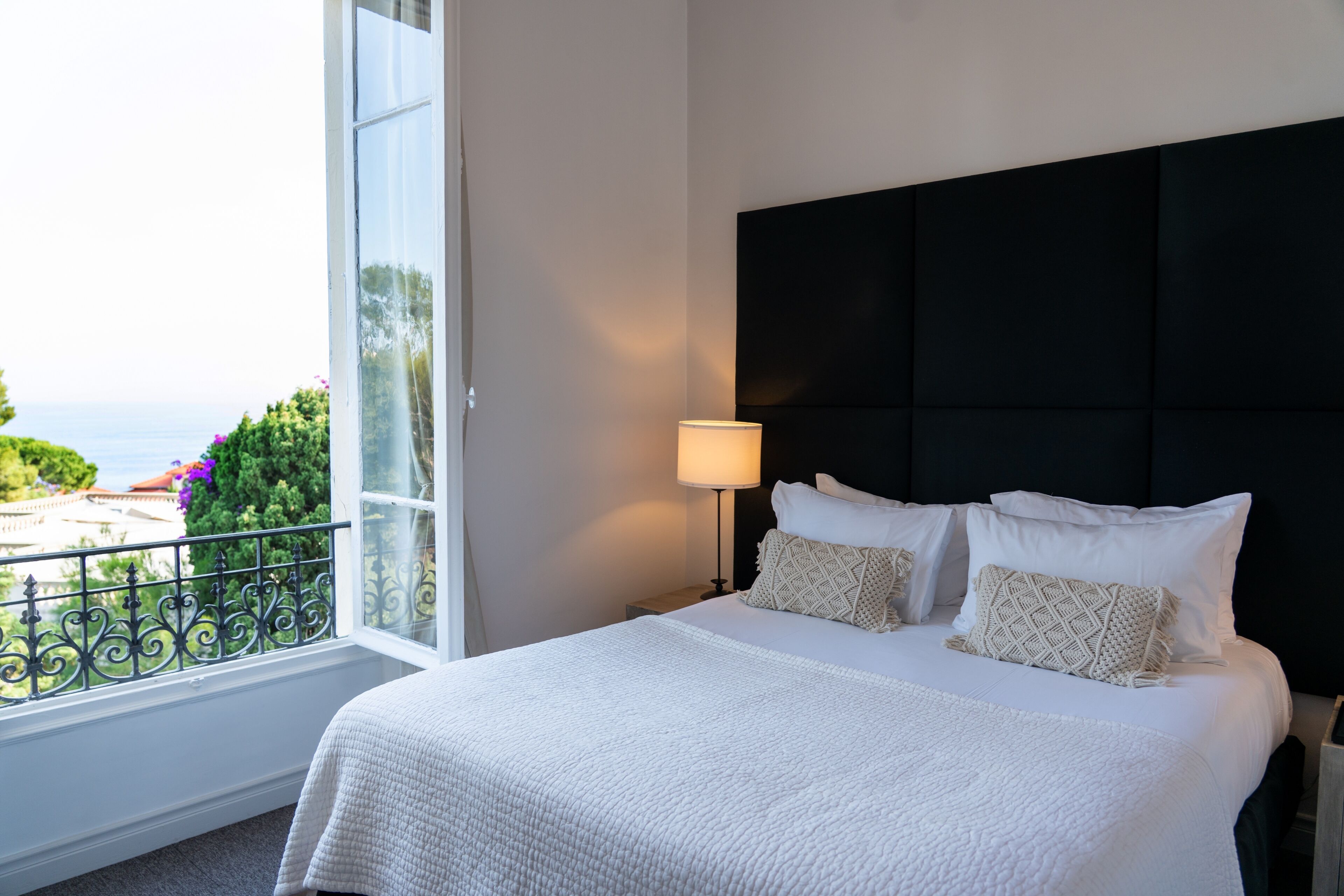 A neatly made bed with white bedding, a black headboard, and a bedside lamp.