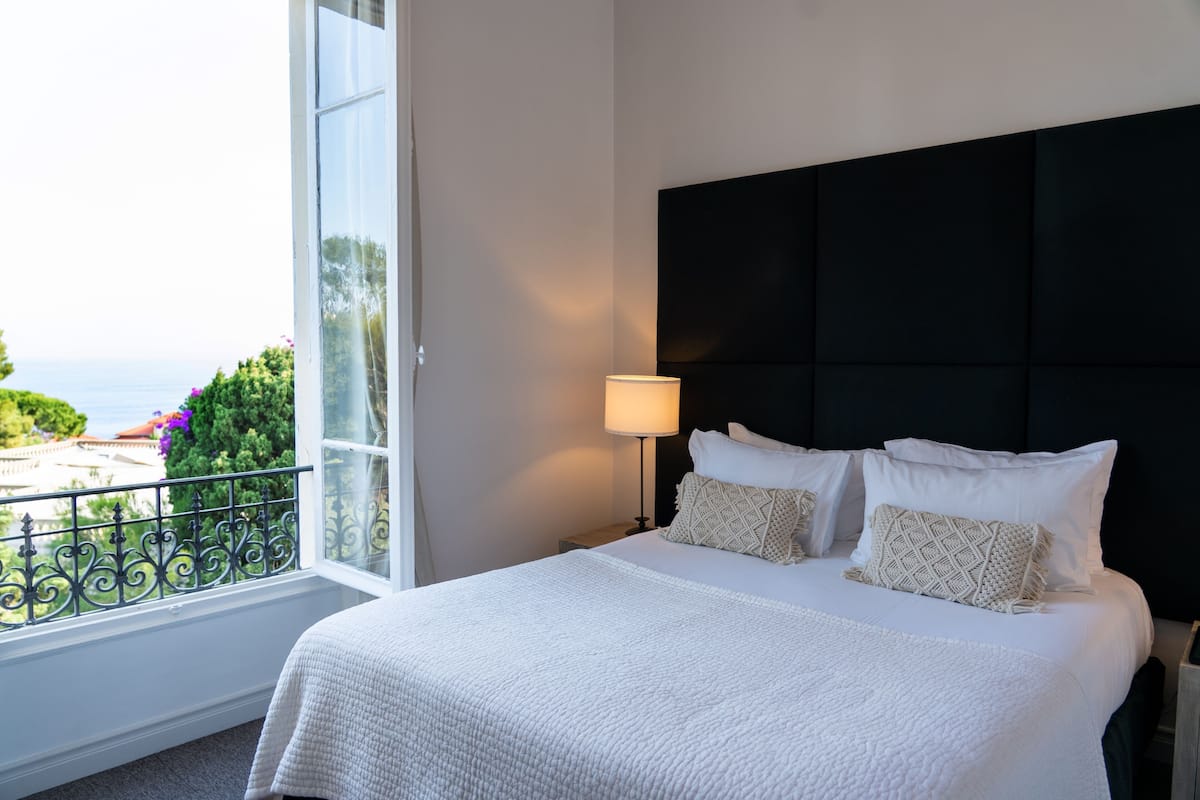 A neatly made bed with white bedding, a black headboard, and a bedside lamp.