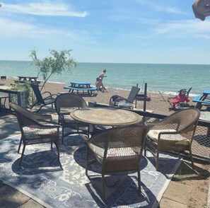A beachside seating area with wicker chairs and a round table, overlooking the sea.