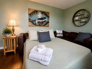 A bedroom with a bed, pillows, a bedside table with a lamp, a wall clock, and a painting. - Amazing Beachfront Cottage with Barbecue in Leamington, Ontario (Leamington)