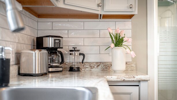 A kitchen with a coffee maker, toaster, blender, and a vase with flowers on the counter. - Amazing Beachfront Cottage with Barbecue in Leamington, Ontario (Leamington)
