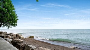 A beach with a wooden walkway, rocky shoreline, and a tree. - Amazing Beachfront Cottage with Barbecue in Leamington, Ontario (Leamington)