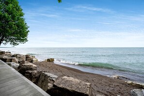 A beach with a wooden walkway, rocky shoreline, and a tree. - Amazing Beachfront Cottage with Barbecue in Leamington, Ontario (Leamington)