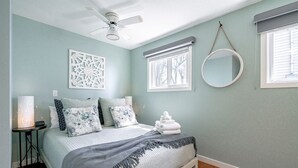 A bedroom with a bed, a ceiling fan, a decorative wall panel, a round mirror, and a window with blinds. - Amazing Beachfront Cottage with Barbecue in Leamington, Ontario (Leamington)