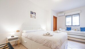 Ein helles Schlafzimmer mit Bett, Nachttisch und einem Fenster mit Vorhängen.